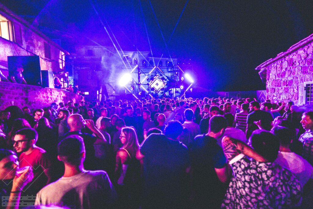 Persone che ballano in una piazzetta medievale nel borgo di Civitella D'Agliano, nel festival di Piazzetta Discoteque.