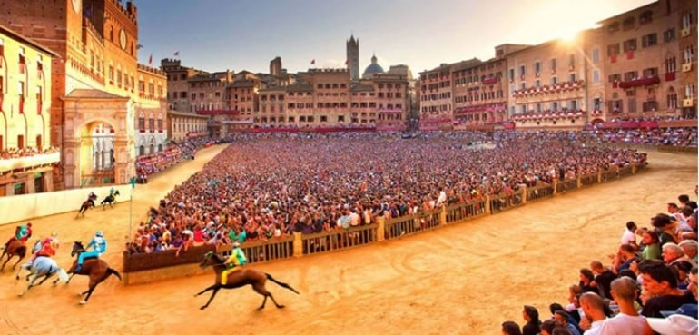 Questa immagine ci raffigura il luogo dove viene svolto il palio di Siena con cavalli in corsa e le persone che tifano la loro contrada.